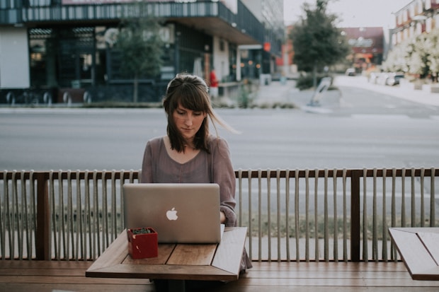 woman in gray shirt sitting on bench in front of MacBook